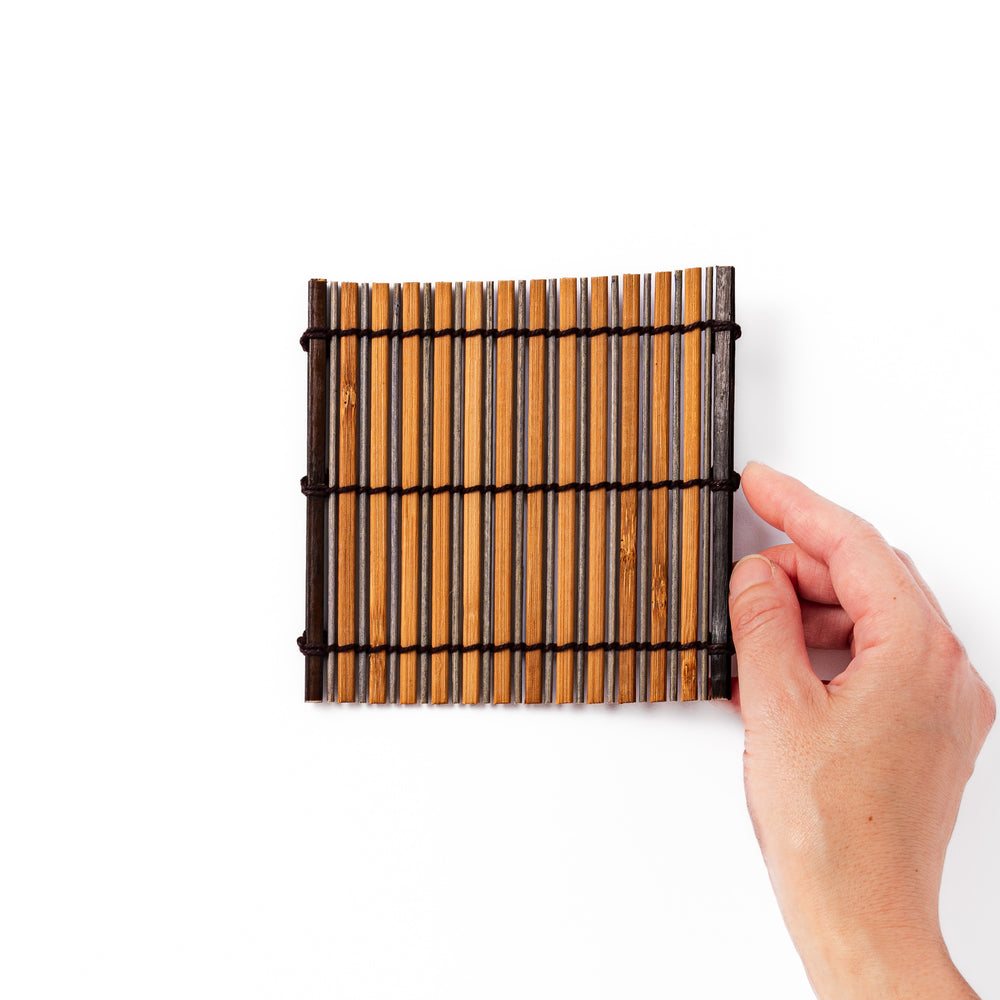 Brown bamboo coaster with alternating natural and dark slats, bound with black cord, adding a rustic and refined touch to Japanese-style tableware.