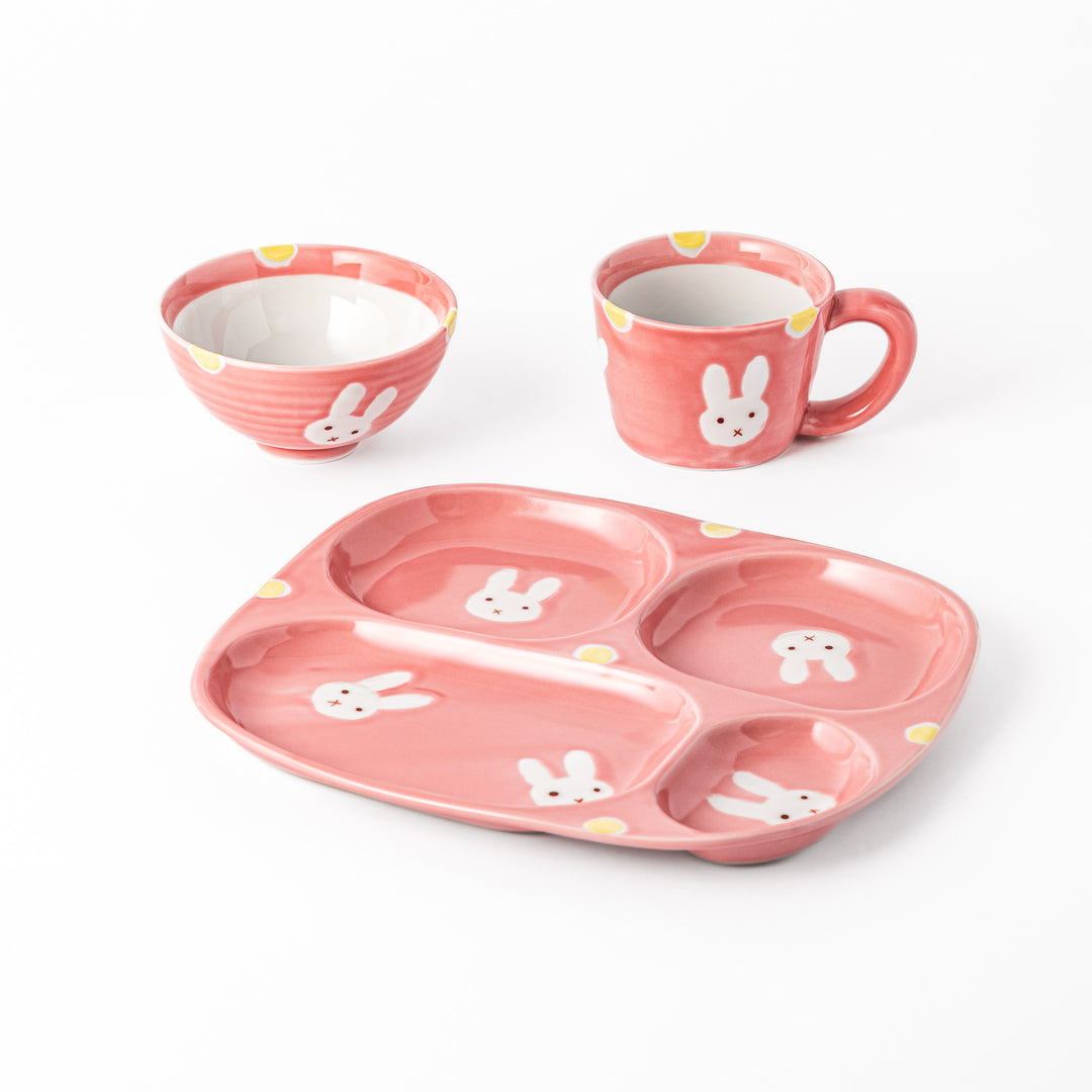 Playful kids' dining set featuring a bunny-themed plate, bowl, and cup, all in a soft pink hue with cute bunny illustrations and yellow accents.