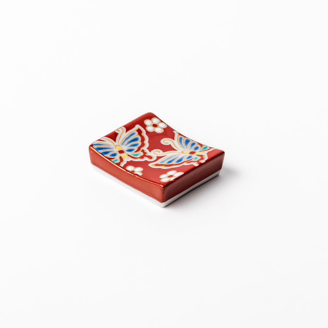Japanese ceramic chopstick rest decorated with colorful butterflies and white blossoms on a vivid red background, adding charm to traditional table settings.