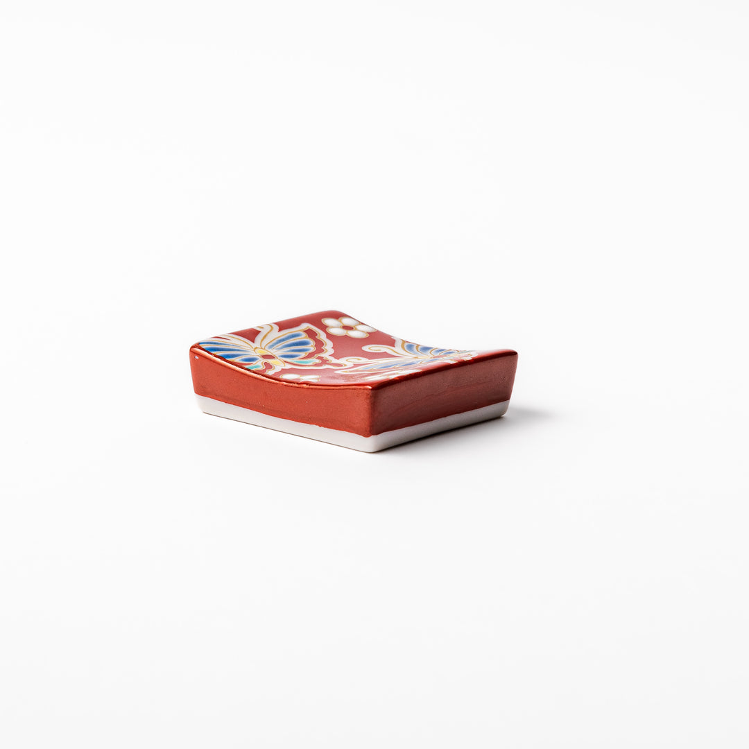 Japanese ceramic chopstick rest decorated with colorful butterflies and white blossoms on a vivid red background, adding charm to traditional table settings.