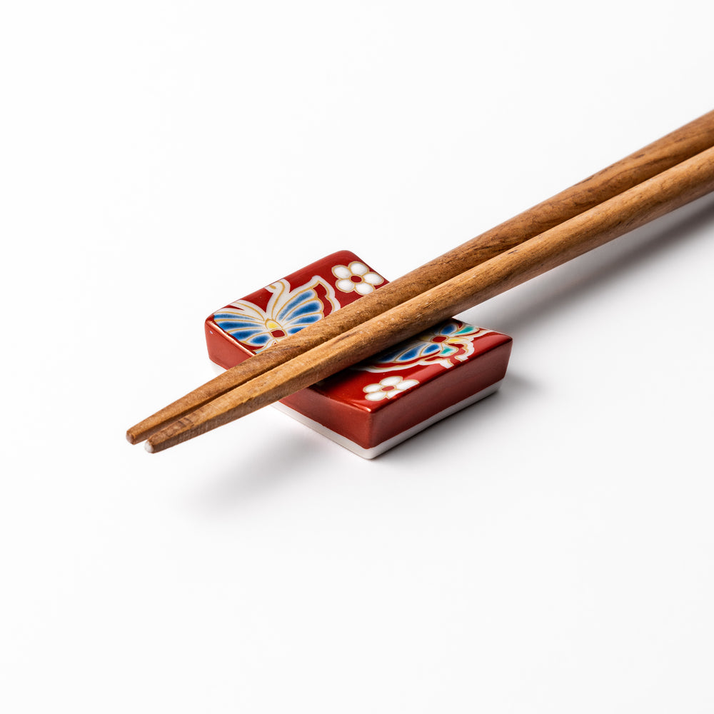 Japanese ceramic chopstick rest decorated with colorful butterflies and white blossoms on a vivid red background, adding charm to traditional table settings.