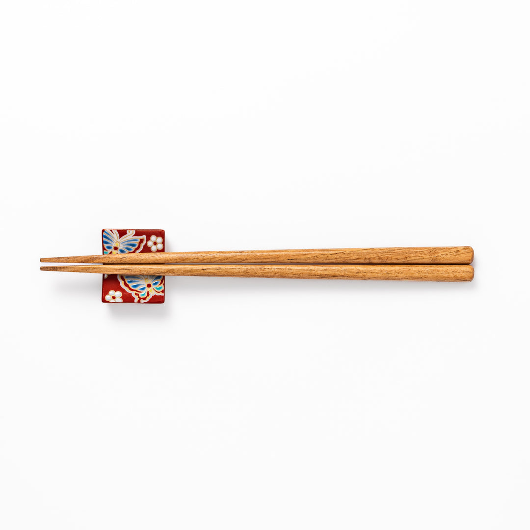 Japanese ceramic chopstick rest decorated with colorful butterflies and white blossoms on a vivid red background, adding charm to traditional table settings.