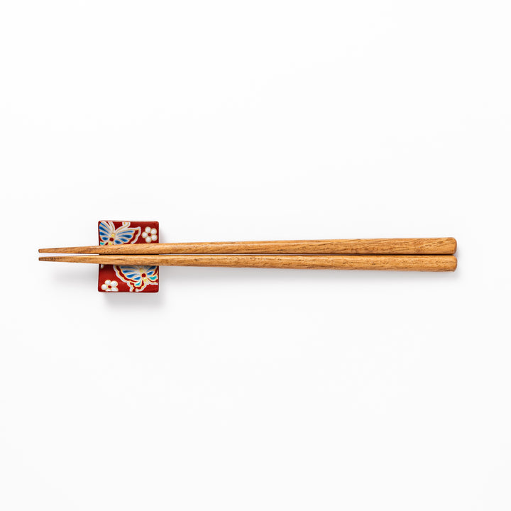 Japanese ceramic chopstick rest decorated with colorful butterflies and white blossoms on a vivid red background, adding charm to traditional table settings.