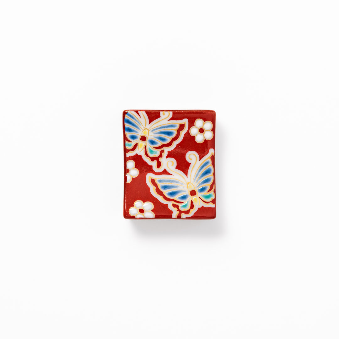 Japanese ceramic chopstick rest decorated with colorful butterflies and white blossoms on a vivid red background, adding charm to traditional table settings.