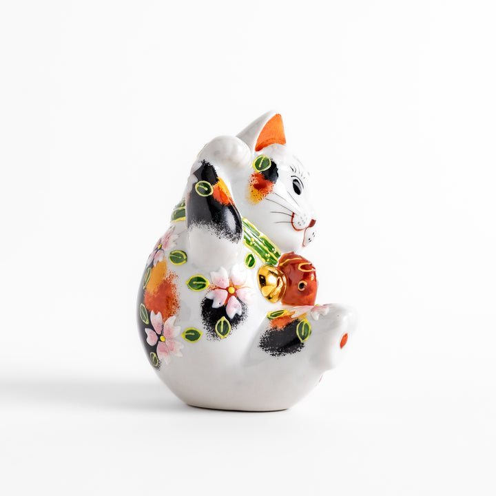 Colorful Calico Maneki Neko figurine holding a lucky sea bream, adorned with floral and green leaf patterns, symbolizing good fortune and prosperity in Japanese culture.