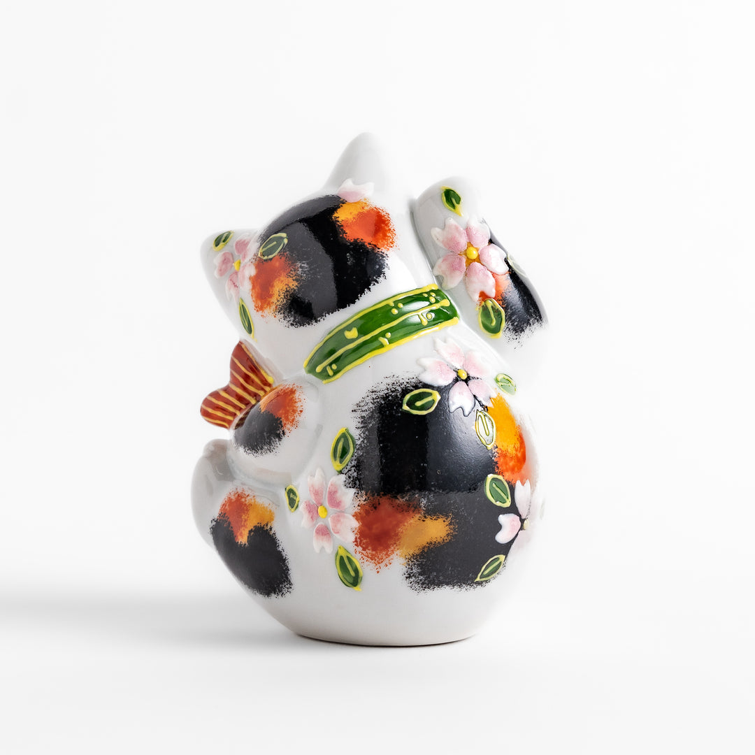 Colorful Calico Maneki Neko figurine holding a lucky sea bream, adorned with floral and green leaf patterns, symbolizing good fortune and prosperity in Japanese culture.