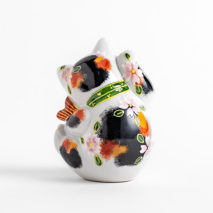 Colorful Calico Maneki Neko figurine holding a lucky sea bream, adorned with floral and green leaf patterns, symbolizing good fortune and prosperity in Japanese culture.