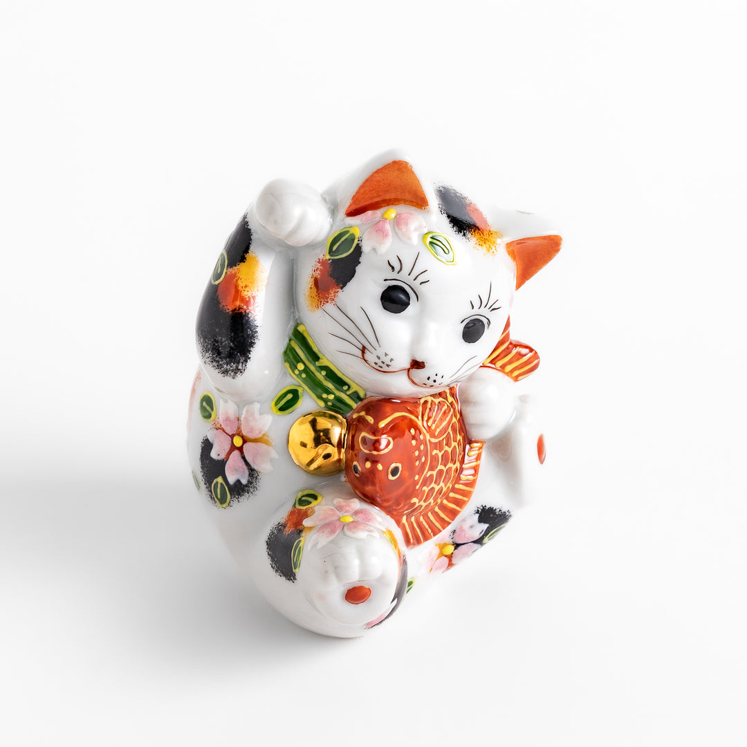 Colorful Calico Maneki Neko figurine holding a lucky sea bream, adorned with floral and green leaf patterns, symbolizing good fortune and prosperity in Japanese culture.