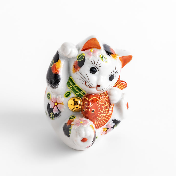Colorful Calico Maneki Neko figurine holding a lucky sea bream, adorned with floral and green leaf patterns, symbolizing good fortune and prosperity in Japanese culture.
