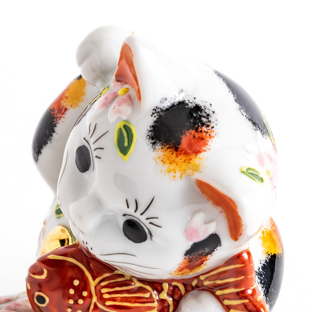 Colorful Calico Maneki Neko figurine holding a lucky sea bream, adorned with floral and green leaf patterns, symbolizing good fortune and prosperity in Japanese culture.