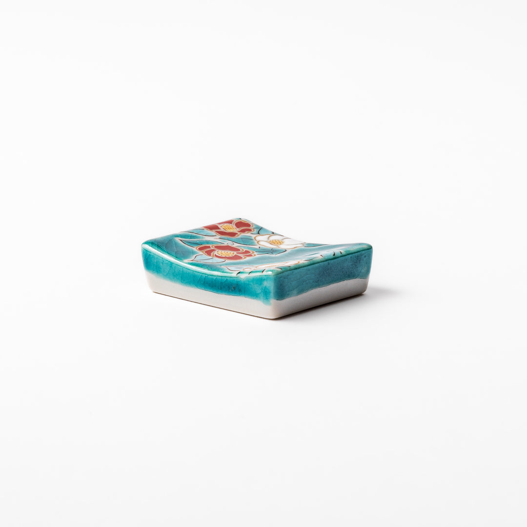 Japanese ceramic chopstick rest featuring red and white camellia blossom design on a glossy teal background, perfect for enhancing elegant table settings.