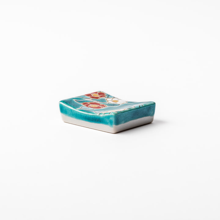 Japanese ceramic chopstick rest featuring red and white camellia blossom design on a glossy teal background, perfect for enhancing elegant table settings.