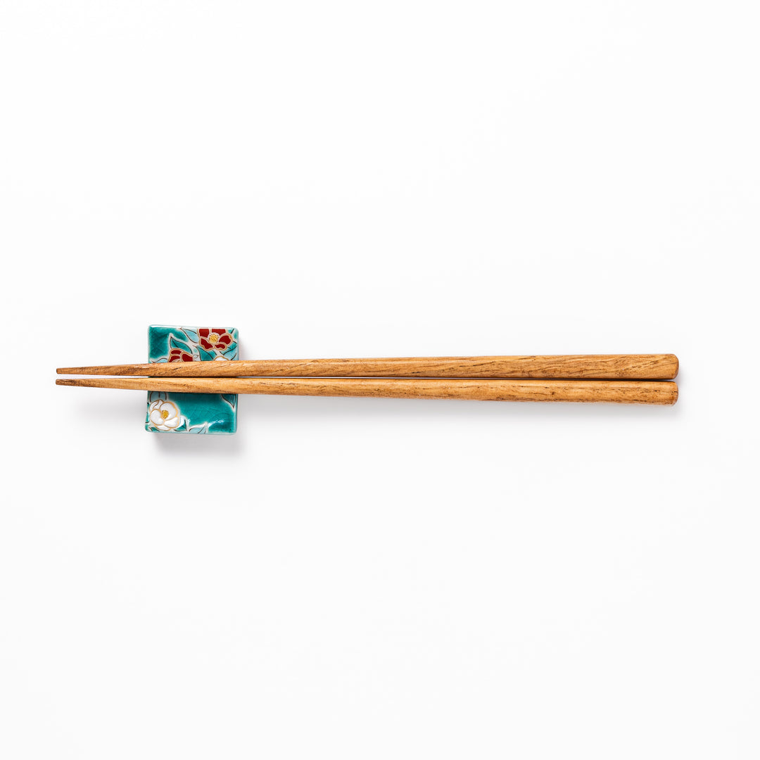 Japanese ceramic chopstick rest featuring red and white camellia blossom design on a glossy teal background, perfect for enhancing elegant table settings.