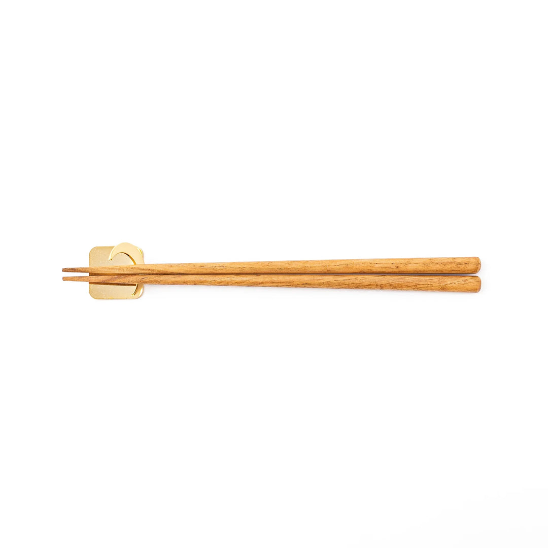 Wooden chopsticks resting on a celestial gold crescent moon chopstick holder minimalist Japanese table setting hashioki