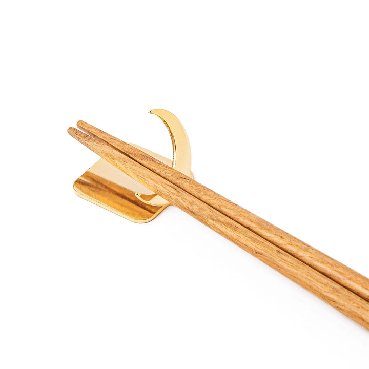 Wooden chopsticks resting on a celestial gold crescent moon chopstick holder minimalist Japanese table setting hashioki
