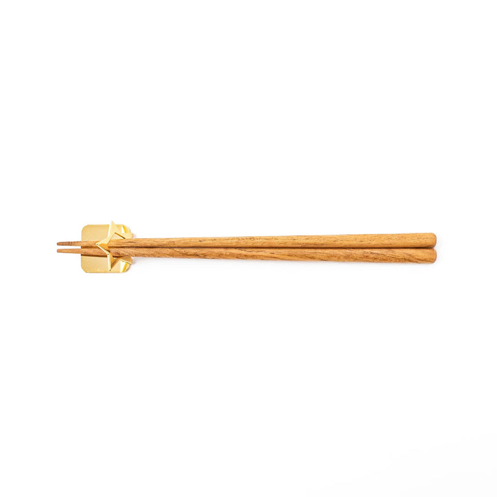 Wooden chopsticks resting on a celestial gold star chopstick holder minimalist Japanese table setting hashioki