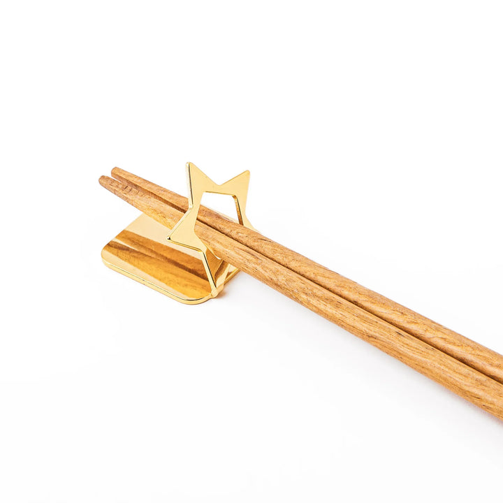 Wooden chopsticks resting on a celestial gold star chopstick holder minimalist Japanese table setting hashioki
