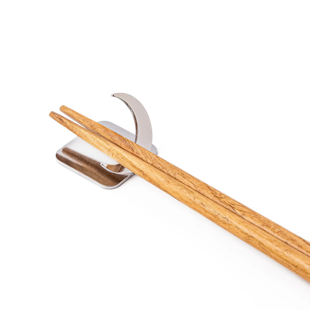 Wooden chopsticks resting on a celestial silver crescent moon chopstick holder minimalist Japanese table setting hashioki