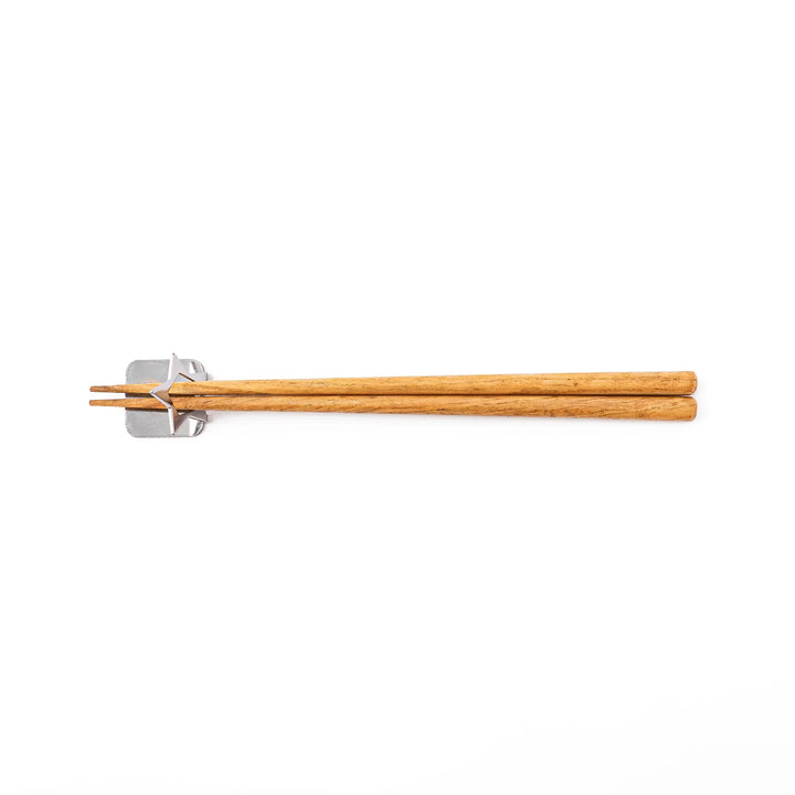 Wooden chopsticks resting on a celestial silver star chopstick holder minimalist Japanese table setting hashioki