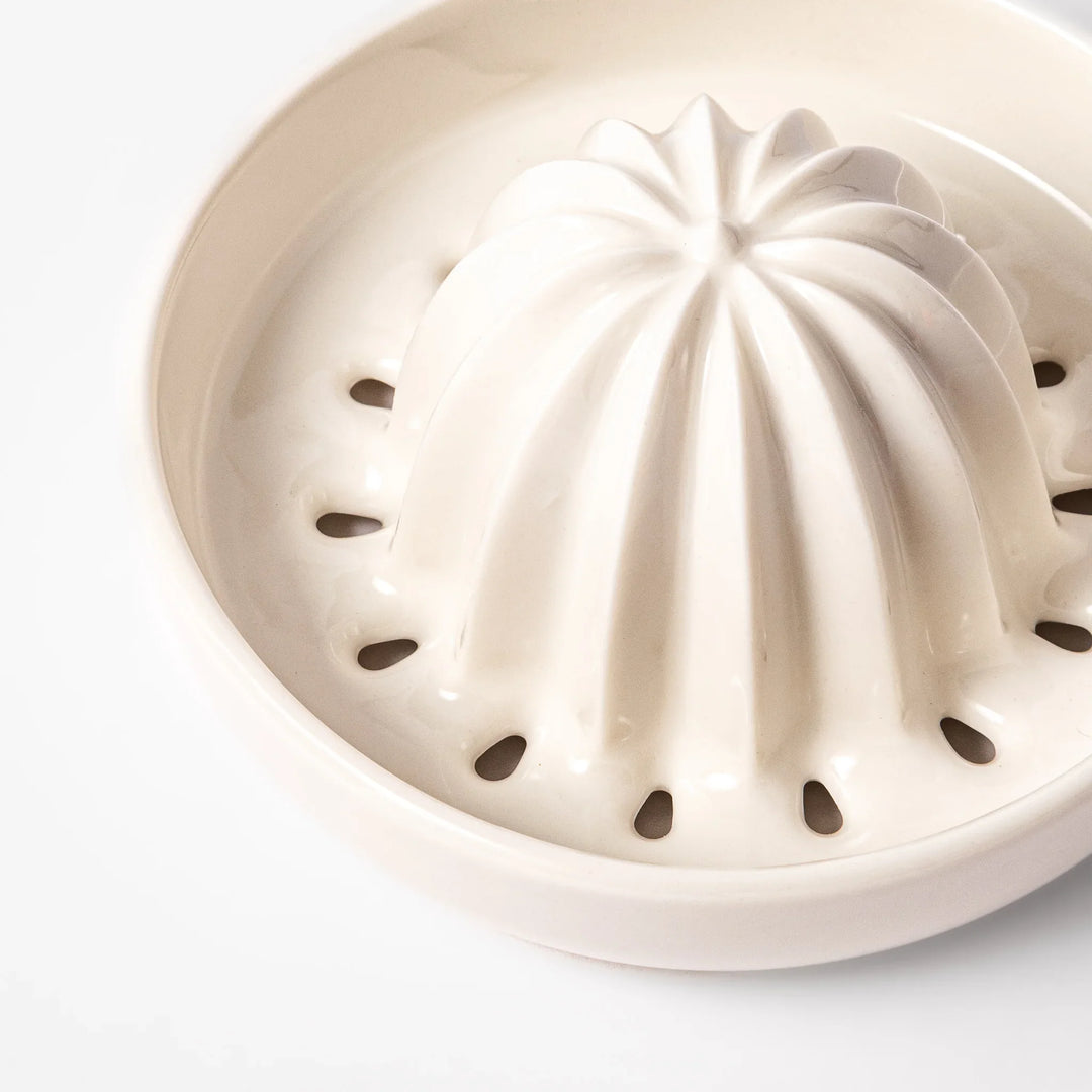 White ceramic citrus juicer with ridged reamer and built-in strainer, designed for effortlessly extracting juice from lemons, limes, and other citrus fruits.