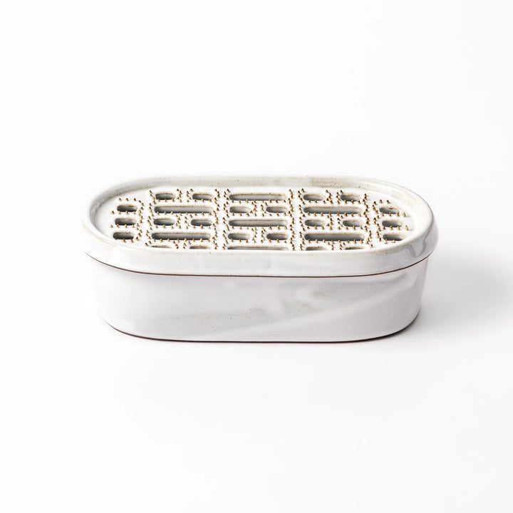 White ceramic daikon oroshi grater with built-in dish and wide grating holes, perfect for smoothly preparing grated daikon, ginger, or root vegetables.