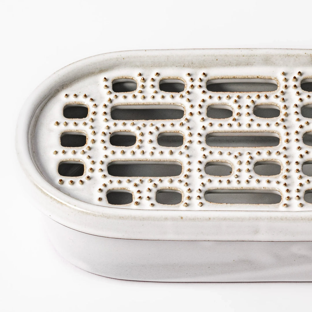 White ceramic daikon oroshi grater with built-in dish and wide grating holes, perfect for smoothly preparing grated daikon, ginger, or root vegetables.