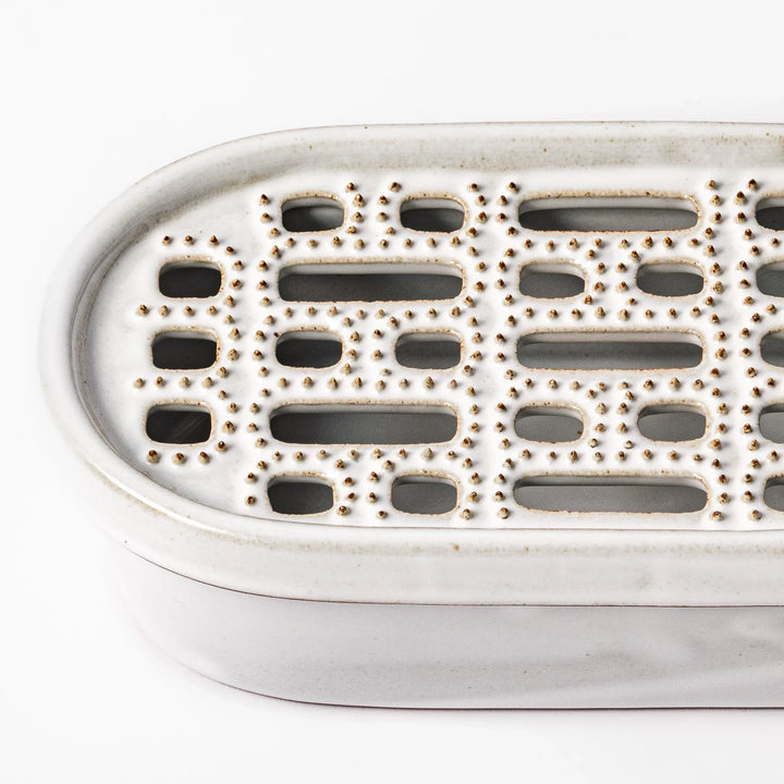 White ceramic daikon oroshi grater with built-in dish and wide grating holes, perfect for smoothly preparing grated daikon, ginger, or root vegetables.