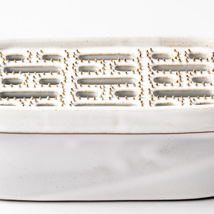 White ceramic daikon oroshi grater with built-in dish and wide grating holes, perfect for smoothly preparing grated daikon, ginger, or root vegetables.