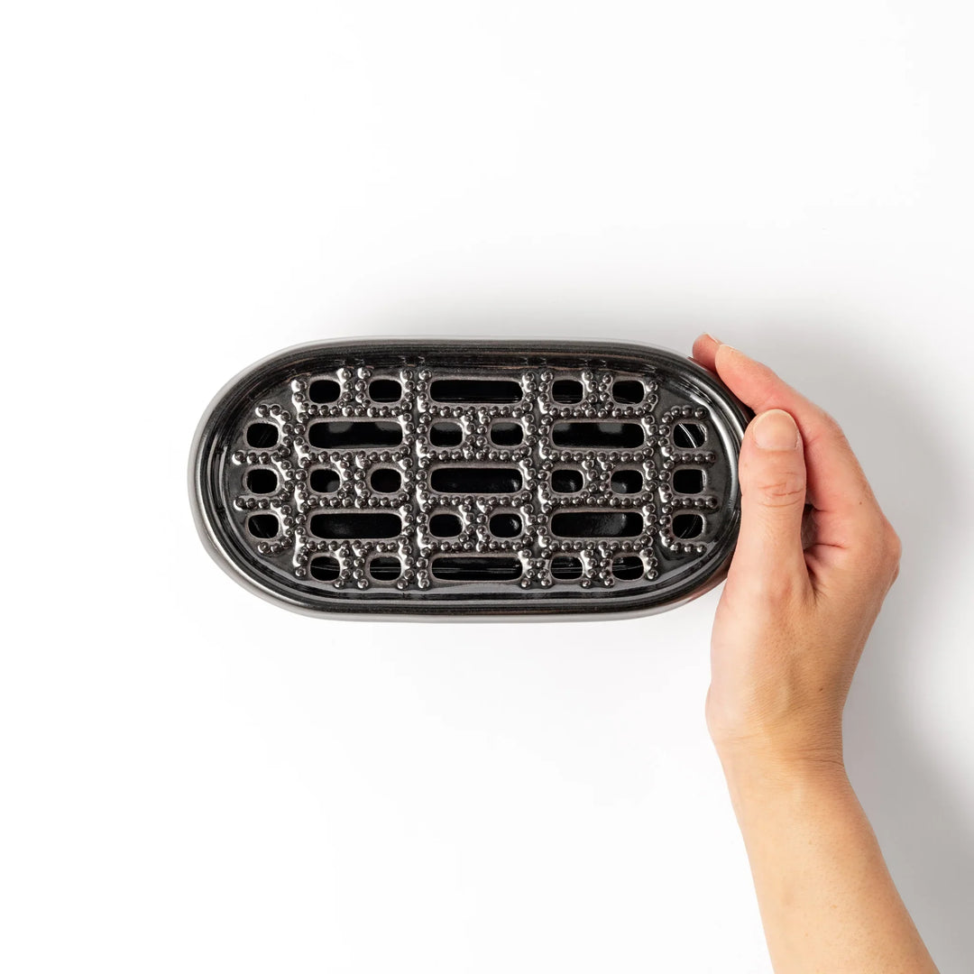 Black ceramic daikon oroshi grater with built-in serving dish, featuring wide grating holes and textured surface for smooth grating and easy cleanup.