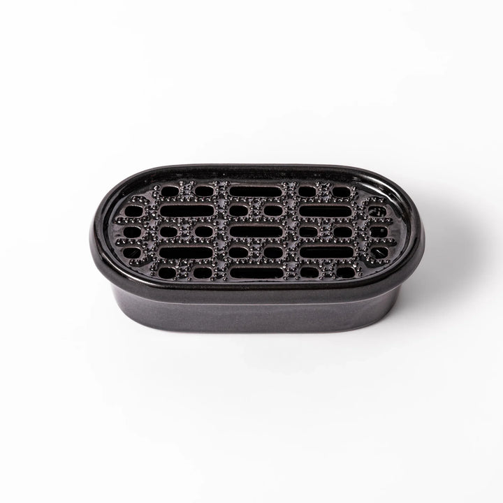 Black ceramic daikon oroshi grater with built-in serving dish, featuring wide grating holes and textured surface for smooth grating and easy cleanup.