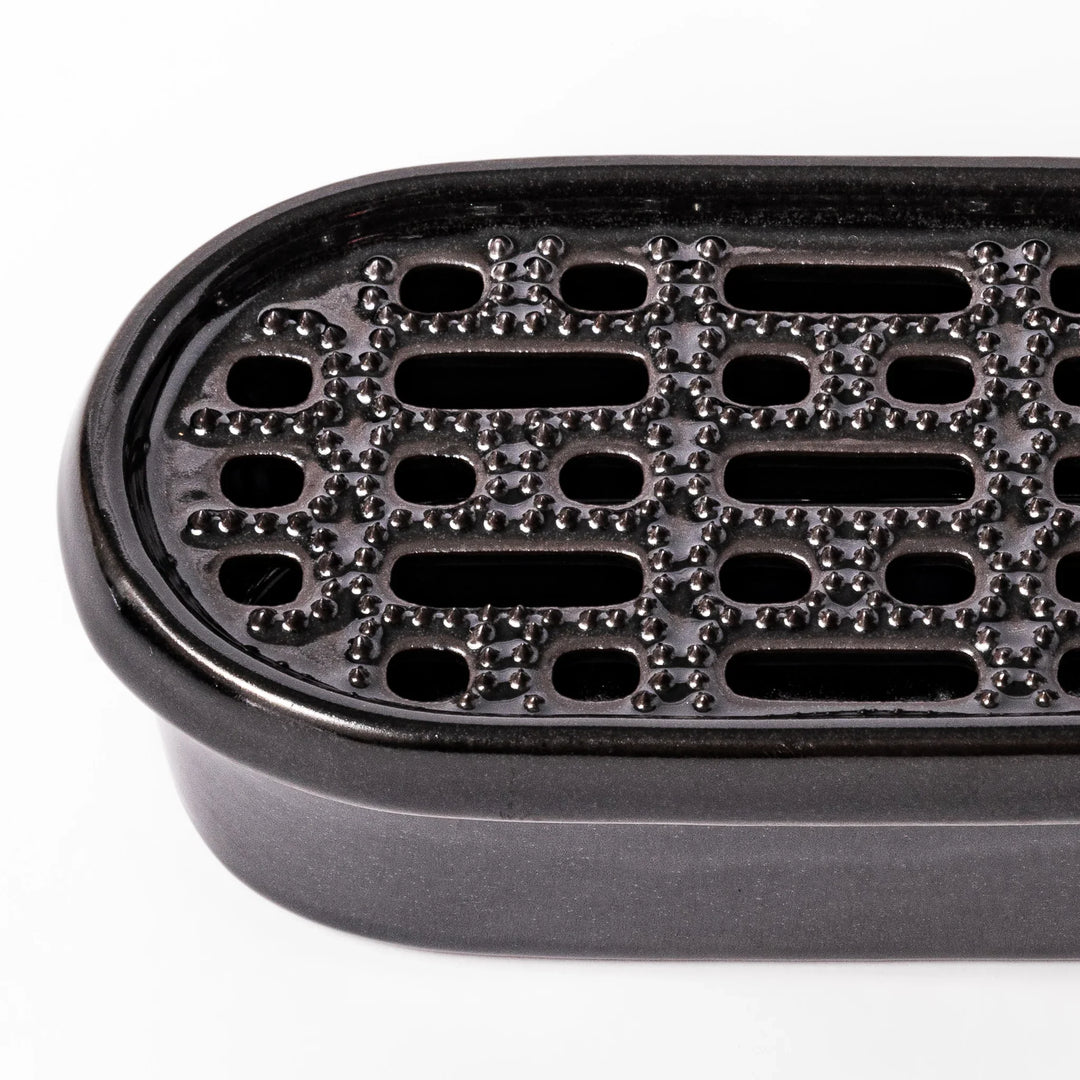 Black ceramic daikon oroshi grater with built-in serving dish, featuring wide grating holes and textured surface for smooth grating and easy cleanup.