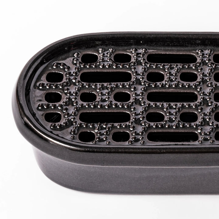 Black ceramic daikon oroshi grater with built-in serving dish, featuring wide grating holes and textured surface for smooth grating and easy cleanup.