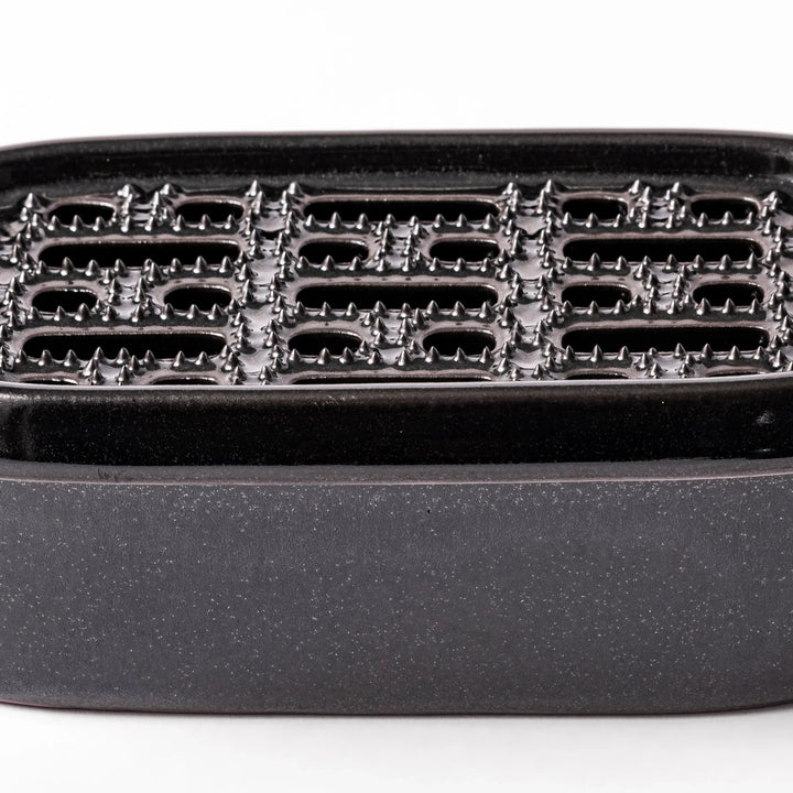 Black ceramic daikon oroshi grater with built-in serving dish, featuring wide grating holes and textured surface for smooth grating and easy cleanup.