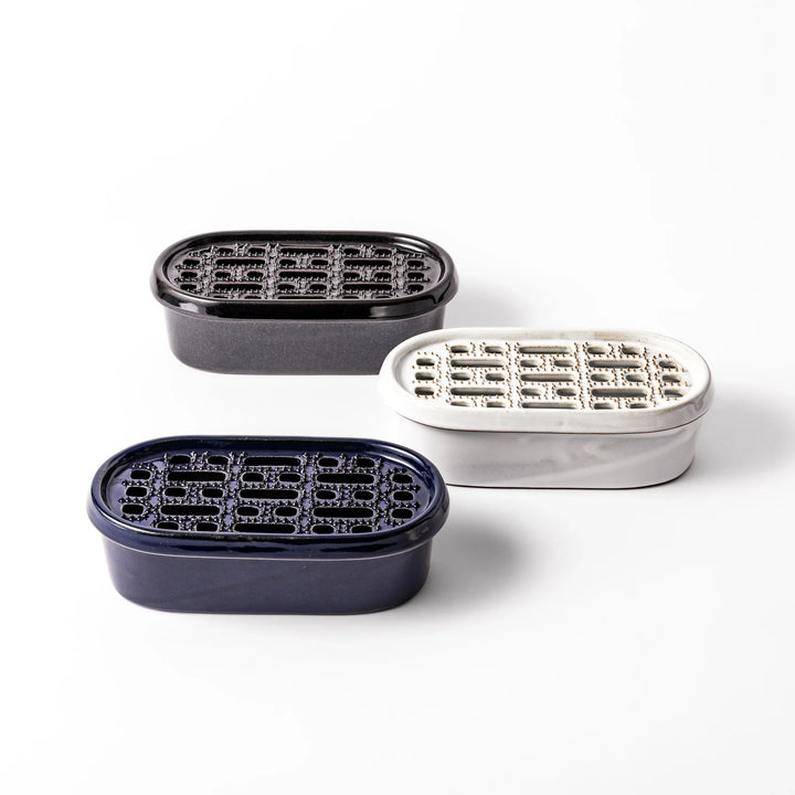 Set of three ceramic daikon oroshi graters with serving dishes in black, white, and deep blue, each featuring wide grating holes for smooth prep.