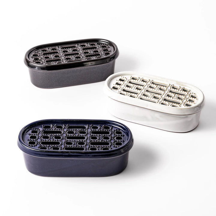 Set of three ceramic daikon oroshi graters with serving dishes in black, white, and deep blue, each featuring wide grating holes for smooth prep.