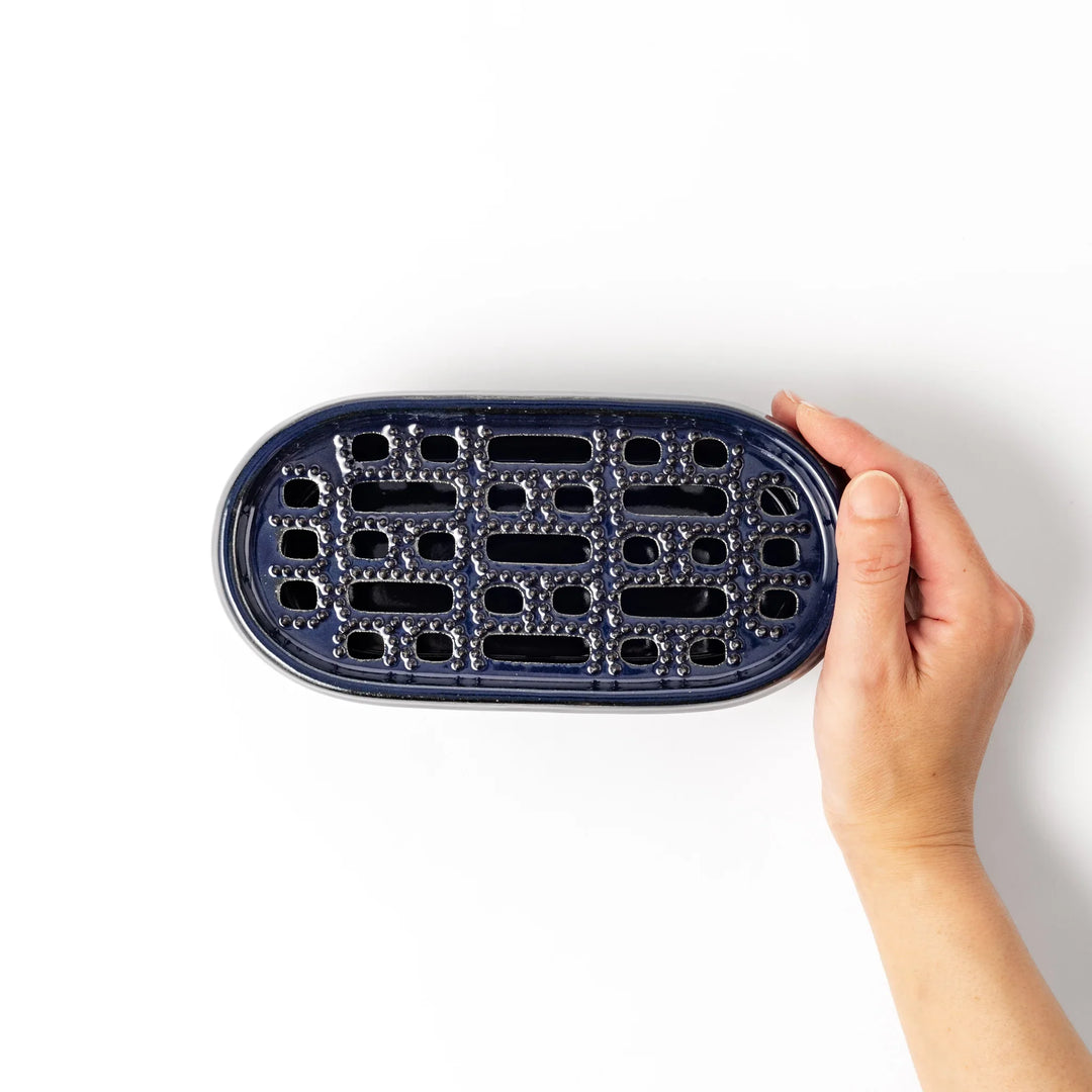 Deep blue ceramic daikon oroshi grater with an integrated serving dish, featuring wide grating holes and raised texture for easy grating and cleanup.