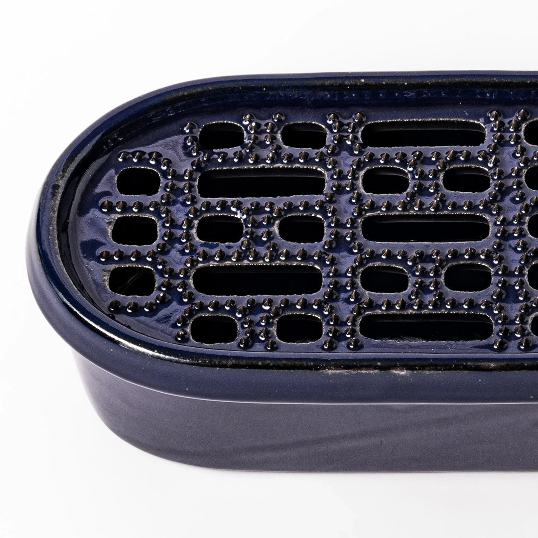 Deep blue ceramic daikon oroshi grater with an integrated serving dish, featuring wide grating holes and raised texture for easy grating and cleanup.