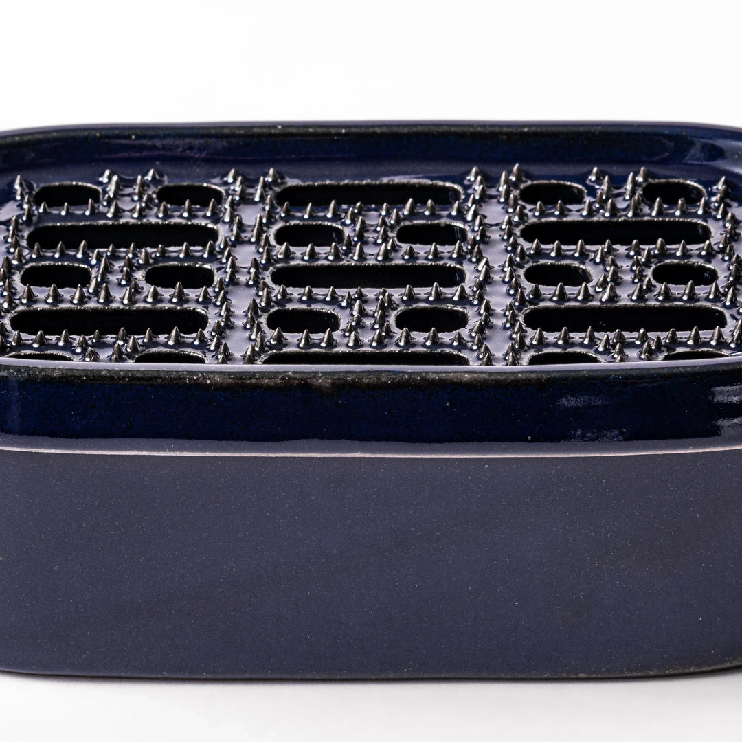 Deep blue ceramic daikon oroshi grater with an integrated serving dish, featuring wide grating holes and raised texture for easy grating and cleanup.