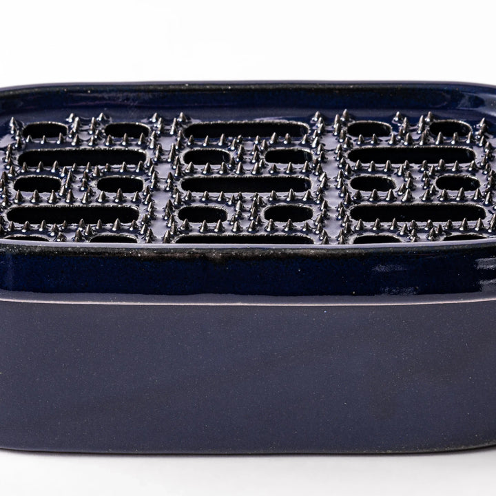 Deep blue ceramic daikon oroshi grater with an integrated serving dish, featuring wide grating holes and raised texture for easy grating and cleanup.