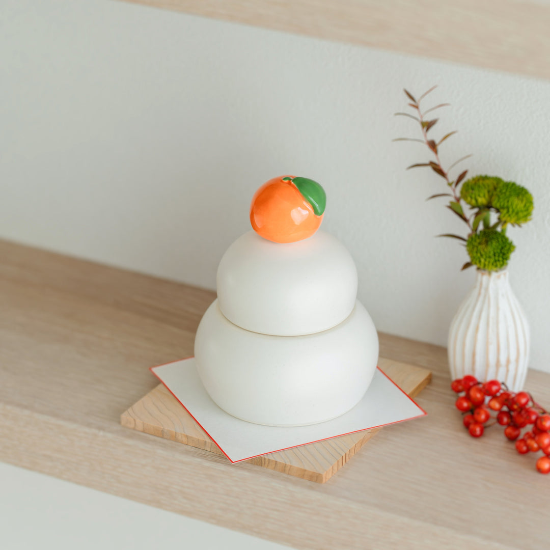 Top view of a white ceramic Kagami Mochi decorative container with an orange lid displayed on a wooden coaster