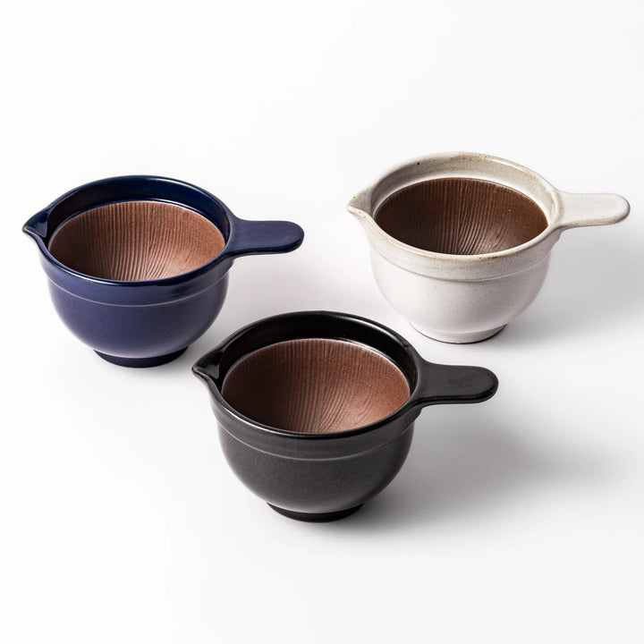 Three ceramic natto suribachi bowls in deep blue, black, and white, each with a ridged brown interior and side handle for easy grinding.









