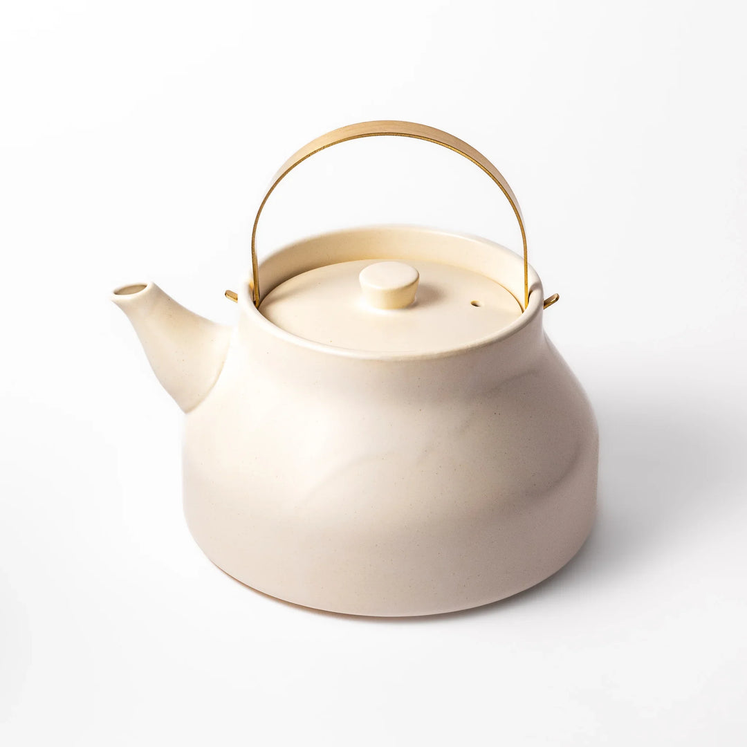 White ceramic stovetop kettle with a smooth matte finish and brass handle, blending traditional charm with modern function for daily tea rituals.