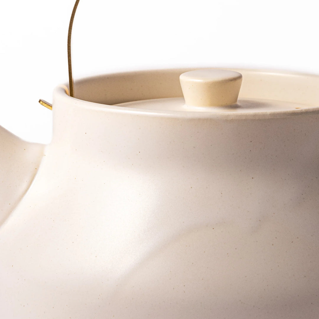 White ceramic stovetop kettle with a smooth matte finish and brass handle, blending traditional charm with modern function for daily tea rituals.