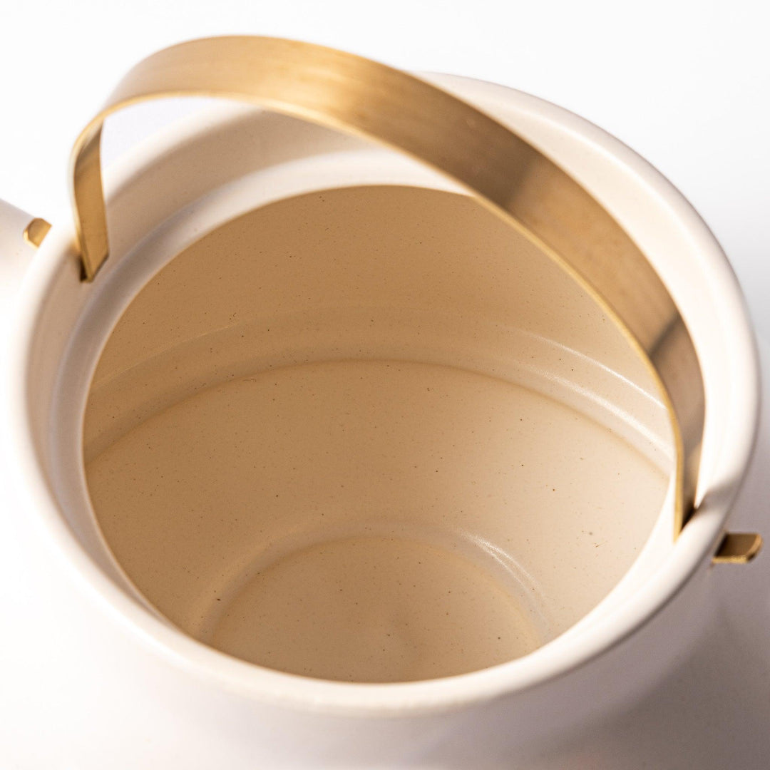 White ceramic stovetop kettle with a smooth matte finish and brass handle, blending traditional charm with modern function for daily tea rituals.