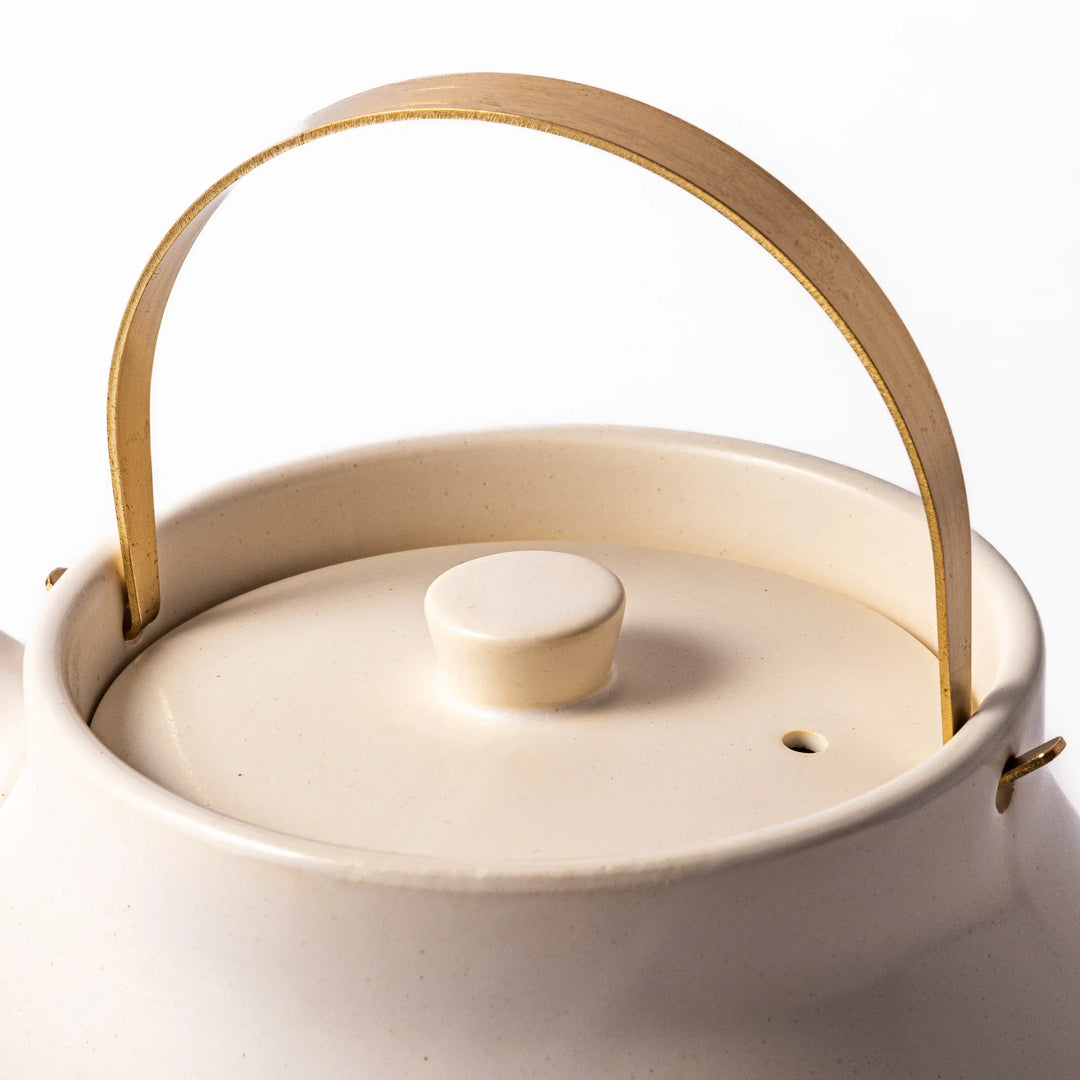 White ceramic stovetop kettle with a smooth matte finish and brass handle, blending traditional charm with modern function for daily tea rituals.