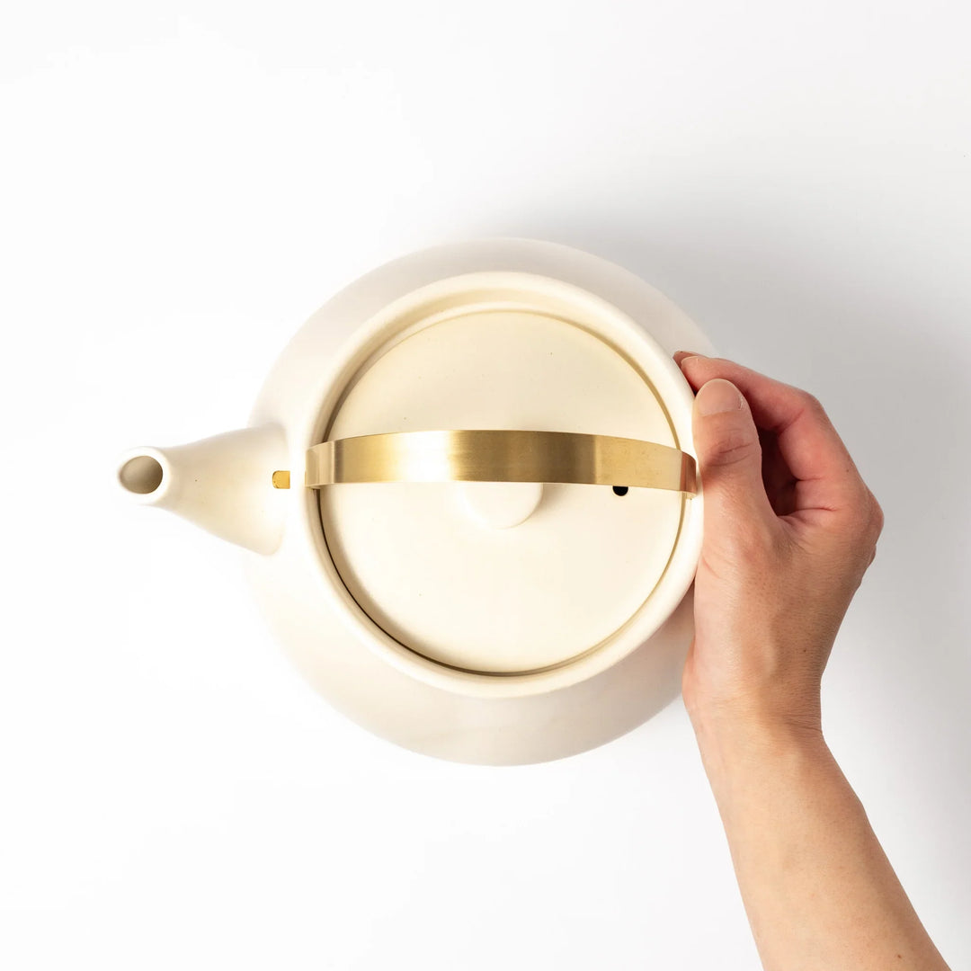 White ceramic stovetop kettle with a smooth matte finish and brass handle, blending traditional charm with modern function for daily tea rituals.