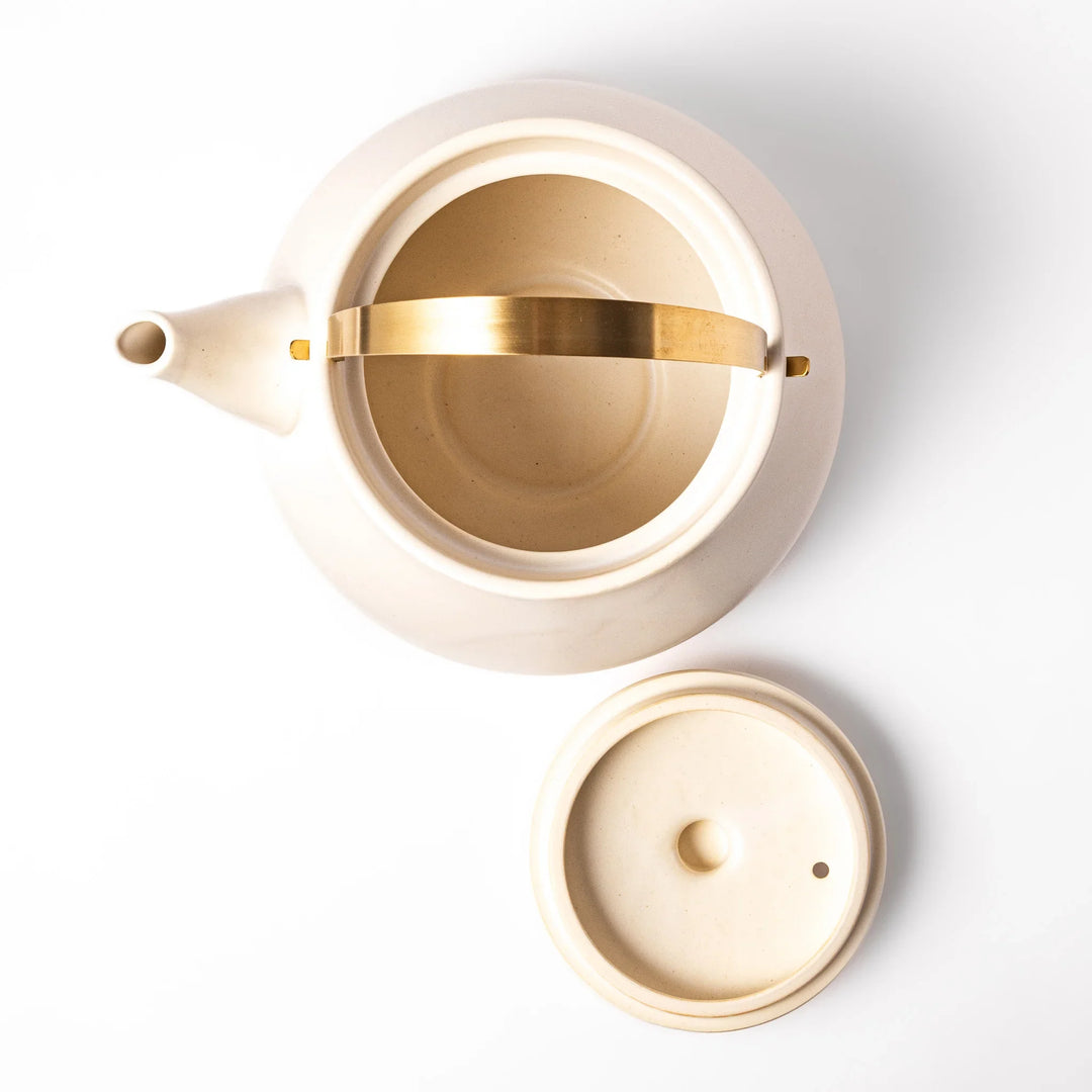 White ceramic stovetop kettle with a smooth matte finish and brass handle, blending traditional charm with modern function for daily tea rituals.