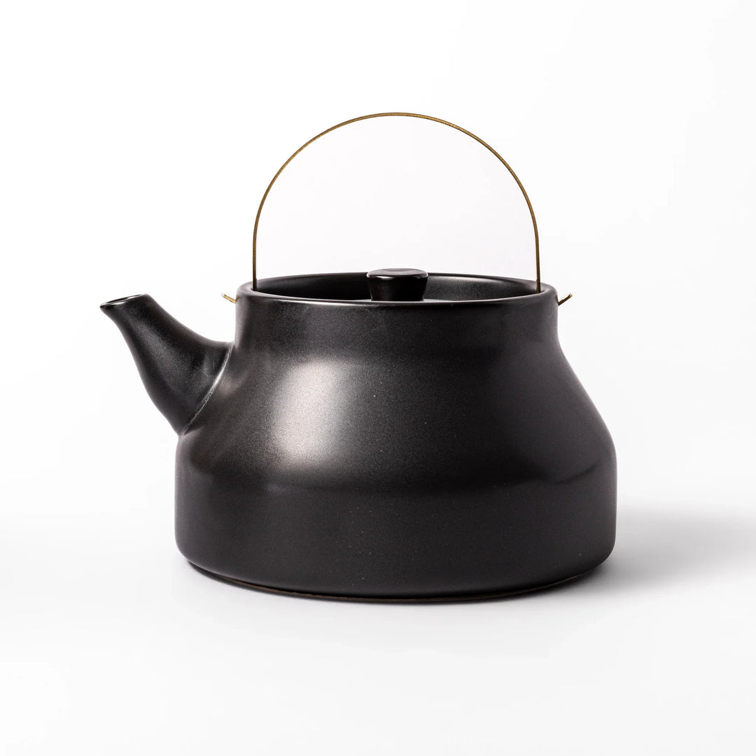 Black ceramic stovetop kettle with a curved silhouette and sleek brass handle, perfect for brewing tea with both elegance and everyday function.