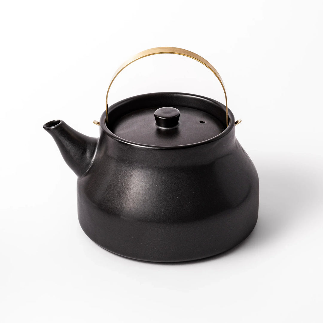 Black ceramic stovetop kettle with a curved silhouette and sleek brass handle, perfect for brewing tea with both elegance and everyday function.