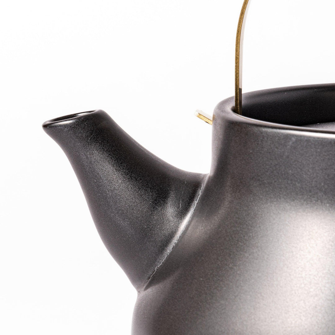 Black ceramic stovetop kettle with a curved silhouette and sleek brass handle, perfect for brewing tea with both elegance and everyday function.